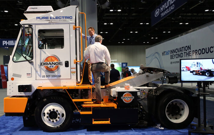 Two casually dressed men are examining an Orange EV electric truck at an expo