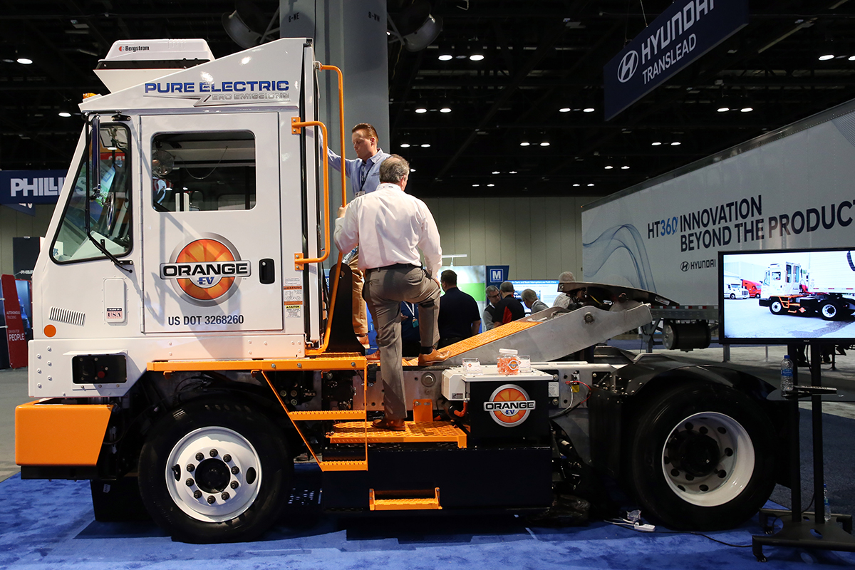 Two casually dressed men are examining an Orange EV electric truck at an expo