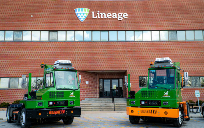 Two green electric yard trucks at Lineage sites