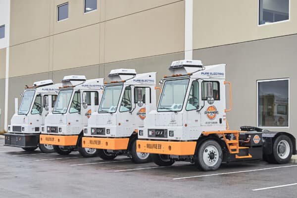 4 white and orange Orange EV yard trucks are parked next to each other outside